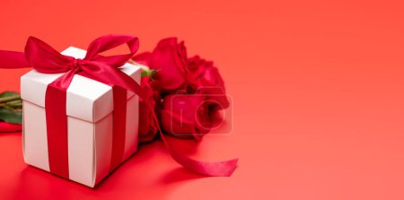 Foto de Tarjeta de San Valentín con caja de regalo y flores rosadas. Sobre fondo rojo con espacio para tus saludos - Imagen libre de derechos