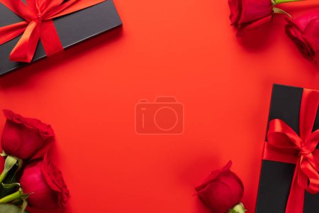 Foto de Tarjeta de San Valentín con cajas de regalo y flores rosadas. Sobre fondo rojo con espacio para tus saludos - Imagen libre de derechos