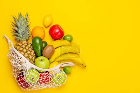 Téléchargez les photos : Sac à provisions plein de fruits sains sur fond jaune. Pose plate avec espace de copie - en image libre de droit
