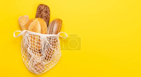 Photo for Fresh baked bread in mesh bag on yellow background. Flat lay with copy space - Royalty Free Image