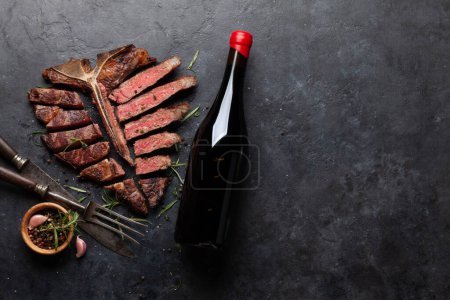 Photo for Grilled porterhouse beef steak and red wine bottle. Sliced T-bone with herbs and spices. Top view flat lay with copy space - Royalty Free Image