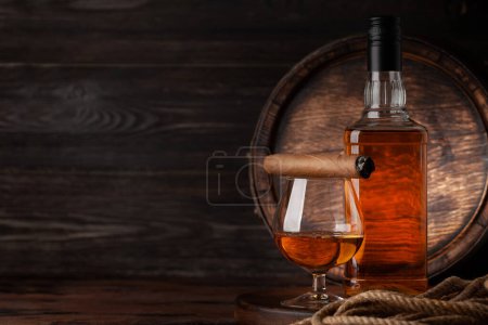 Foto de Vaso y botella con coñac, whisky o ron dorado y cigarro. Delante del viejo barril de madera con espacio para copias - Imagen libre de derechos
