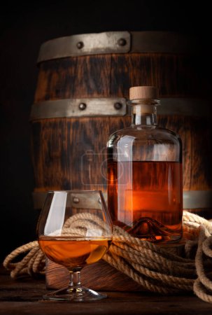 Photo for Glass and bottle with cognac, whiskey or golden rum. In front of old wooden barrel - Royalty Free Image