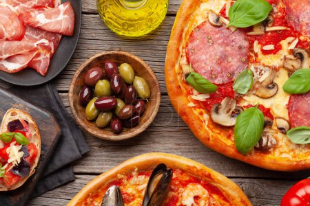 Photo for Italian cuisine. Pepperoni and seafood pizza, olives and antipasto toasts. Flat lay on wooden table - Royalty Free Image