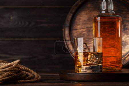 Glass and bottle with cognac, whiskey or golden rum. In front of old wooden barrel with copy space