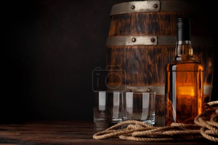 Photo for Glasses and bottle with cognac, whiskey or golden rum. In front of old wooden barrel with copy space - Royalty Free Image