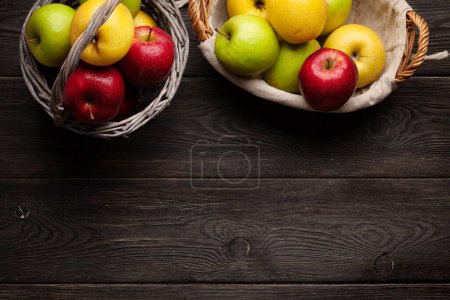 Foto de Coloridos frutos maduros de manzana en cesta sobre mesa de madera. Vista superior plano con espacio de copia - Imagen libre de derechos