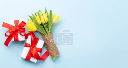 Téléchargez les photos : Bouquet de fleurs de tulipes jaunes et boîtes-cadeaux sur fond bleu. Vue du dessus plat avec espace de copie - en image libre de droit