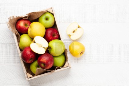 Foto de Coloridos frutos maduros de manzana en caja sobre mesa de madera. Vista superior plano con espacio de copia - Imagen libre de derechos