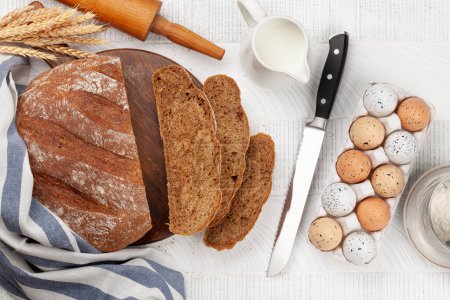 Téléchargez les photos : Trancher le pain fait maison et les ingrédients sur une table en bois. Pose plate - en image libre de droit