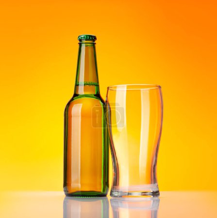 Foto de Botella de cerveza y vaso vacío delante de fondo amarillo. Captura de estudio - Imagen libre de derechos