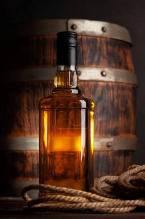 Photo for Bottle with whiskey, cognac or golden rum. In front of old wooden barrel - Royalty Free Image