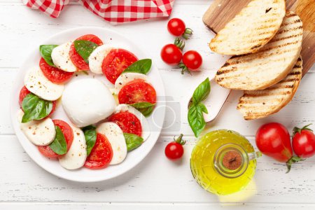 Téléchargez les photos : Salade caprese avec mozzarella, basilic, tomates fraîches de jardin et pain grillé. Vue du dessus plat lay - en image libre de droit