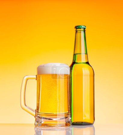 Foto de Botella de cerveza y vaso con cerveza lager delante de fondo amarillo. Captura de estudio - Imagen libre de derechos