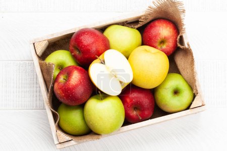 Foto de Coloridos frutos maduros de manzana en caja sobre mesa de madera. Vista superior plano laico - Imagen libre de derechos