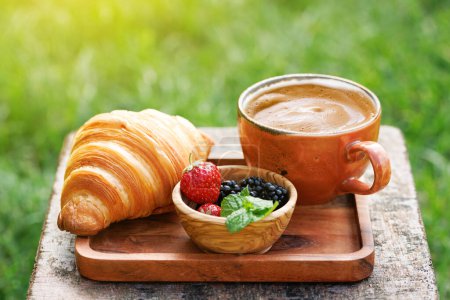 Photo for Coffee cup and croissant on outside garden table. Sunny outdoor meal - Royalty Free Image