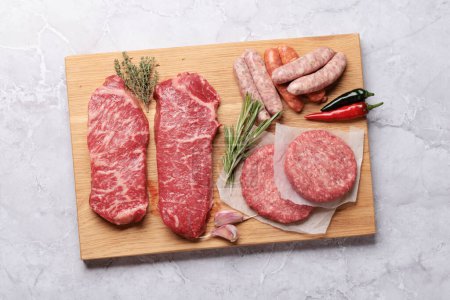 Téléchargez les photos : De la viande crue. Steaks, saucisses, burgers et épices sur planche à découper. Pose plate - en image libre de droit