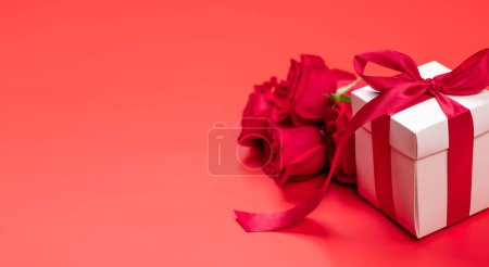 Foto de Tarjeta de San Valentín con caja de regalo y flores rosadas. Sobre fondo rojo con espacio para tus saludos - Imagen libre de derechos