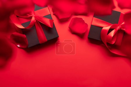 Foto de Tarjeta de San Valentín con cajas de regalo y pétalos de rosa. Sobre fondo rojo con espacio para tus saludos - Imagen libre de derechos