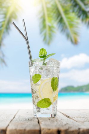 Téléchargez les photos : Cocktail mojito sur table en bois face à la mer ensoleillée et aux feuilles de palmier - en image libre de droit