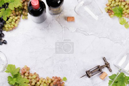 Téléchargez les photos : Verres à vin, bouteilles et raisins sur table en marbre. Pose plate avec espace de copie - en image libre de droit