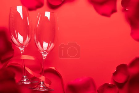 Foto de Tarjeta de San Valentín con copas de champán y pétalos de rosa. Sobre fondo rojo con espacio para tus saludos - Imagen libre de derechos