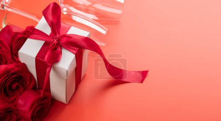 Foto de Tarjeta de San Valentín con copas de champán, flores de rosa y caja de regalo. Sobre fondo rojo con espacio para tus saludos - Imagen libre de derechos