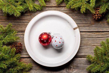 Téléchargez les photos : Cadre de table d'en haut avec des boules sur l'assiette, branches de sapin de Noël et cônes de pin sur fond en bois. Pose plate - en image libre de droit