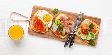 Photo for Breakfast waffles with fried eggs, salmon, bacon, cucumber and prawns. Top view flat lay with orange juice - Royalty Free Image
