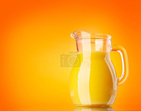 Photo for Fresh orange juice in a glass pitcher over orange background - Royalty Free Image