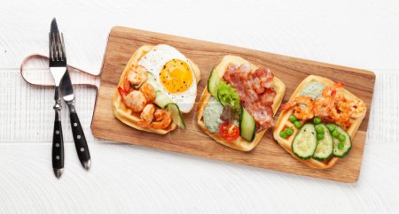 Photo for Breakfast waffles with fried eggs, salmon, bacon, cucumber and prawns. Top view flat lay - Royalty Free Image