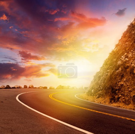 Téléchargez les photos : Route asphaltée vide dans un paysage rural au coucher du soleil avec un ciel spectaculaire - en image libre de droit