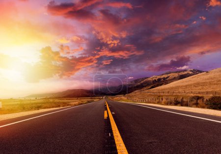 Foto de Camino de asfalto vacío en el paisaje rural al atardecer con cielo dramático - Imagen libre de derechos