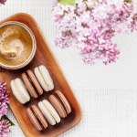 Macaroon cookies and coffee. On wooden table with lilac flowers. Top view flat lay with copy space