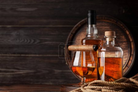 Foto de Vaso y botellas con coñac, whisky o ron dorado y cigarro. Delante del viejo barril de madera con espacio para copias - Imagen libre de derechos