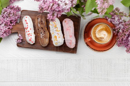 Photo for Eclair dessert and coffee. On wooden table with lilac flowers. Top view flat lay with copy space - Royalty Free Image