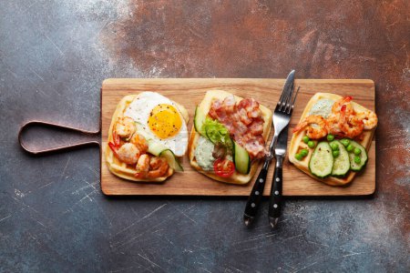 Téléchargez les photos : Gaufres pour le petit déjeuner avec œufs frits, saumon, bacon, concombre et crevettes. Vue du dessus plat avec espace de copie - en image libre de droit