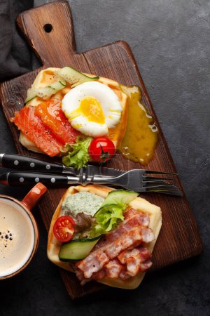 Photo for Breakfast waffles with fried eggs, salmon, bacon, cucumber and prawns. Top view flat lay with coffee - Royalty Free Image