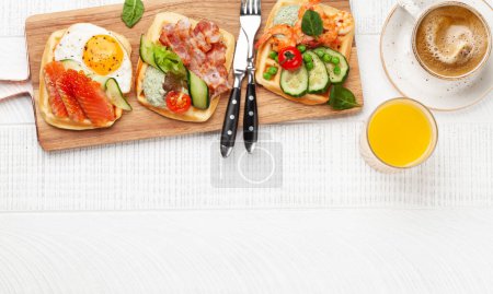 Foto de Desayuno gofres con huevos fritos, salmón, tocino, pepino y gambas. Vista superior plano con café, zumo de naranja y espacio de copia - Imagen libre de derechos