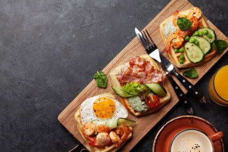 Photo for Breakfast waffles with fried eggs, salmon, bacon, cucumber and prawns. Top view flat lay with coffee, orange juice and copy space - Royalty Free Image
