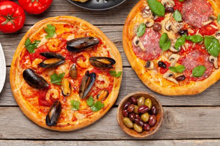 Foto de Cocina italiana. Pizza de pepperoni y mariscos, aceitunas y tostadas antipasto. Colocación plana sobre mesa de madera - Imagen libre de derechos