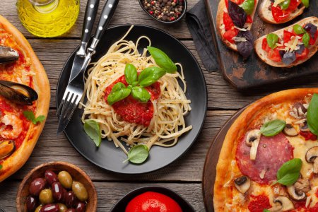 Foto de Cocina italiana. Pastas, pizza, aceitunas y tostadas antipasto. Colocación plana sobre mesa de madera - Imagen libre de derechos