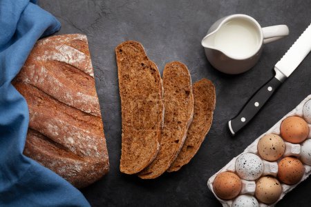 Téléchargez les photos : Trancher le pain fait maison et les ingrédients sur une table en pierre. Pose plate - en image libre de droit