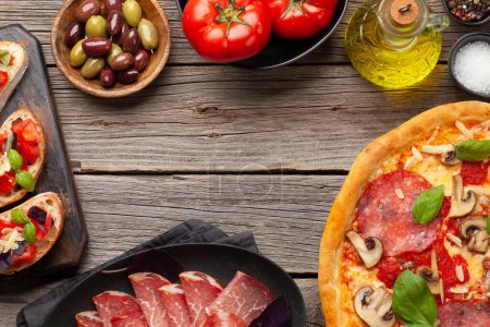 Photo for Italian cuisine. Pepperoni pizza and antipasto toasts. Flat lay on wooden table with copy space - Royalty Free Image