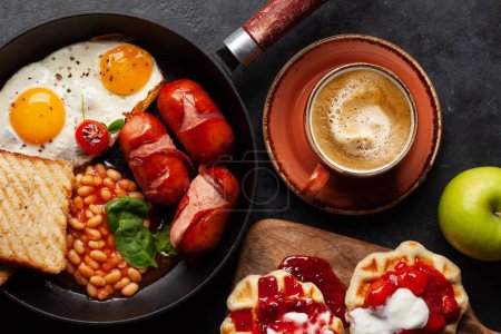 Foto de Desayuno inglés con huevos fritos, frijoles, tocino y salchichas. Café y jugo de naranja. Vista superior plano laico - Imagen libre de derechos