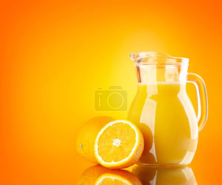 Foto de Jugo de naranja fresco en una jarra de vidrio sobre fondo naranja - Imagen libre de derechos