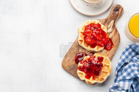 Téléchargez les photos : Gaufres fraîches pour le petit déjeuner avec confiture de baies, café et jus d'orange. Vue du dessus plat avec espace de copie - en image libre de droit
