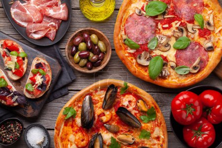 Téléchargez les photos : Cuisine italienne. Pizza aux poivrons et fruits de mer, olives et toasts antipasto. Poser à plat sur une table en bois - en image libre de droit