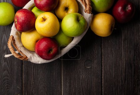 Foto de Coloridos frutos maduros de manzana en cesta sobre mesa de madera. Vista superior plano con espacio de copia - Imagen libre de derechos