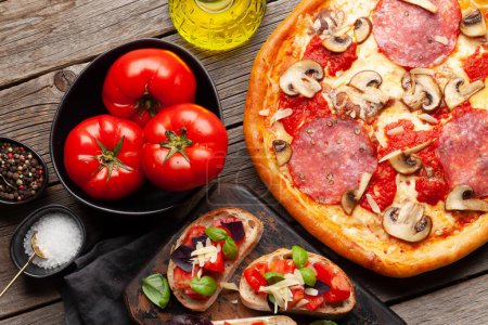 Photo for Italian cuisine. Pepperoni pizza, tomatoes and antipasto toasts. Flat lay on wooden table - Royalty Free Image